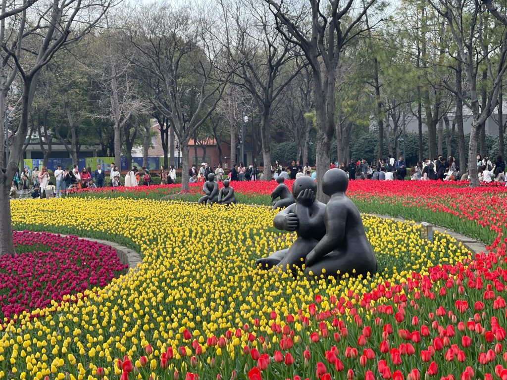 这个雕塑是美国艺术家乔伊・布朗（Joy Brown）的作品，通常被称为《情侣》（也叫《悄悄话》或《相拥》），它坐落在上海静安雕塑公园的郁金香花海旁，以圆润抽象的造型展现了情侣依偎低语的浪漫氛围，是春日赏花时的热门打卡点。