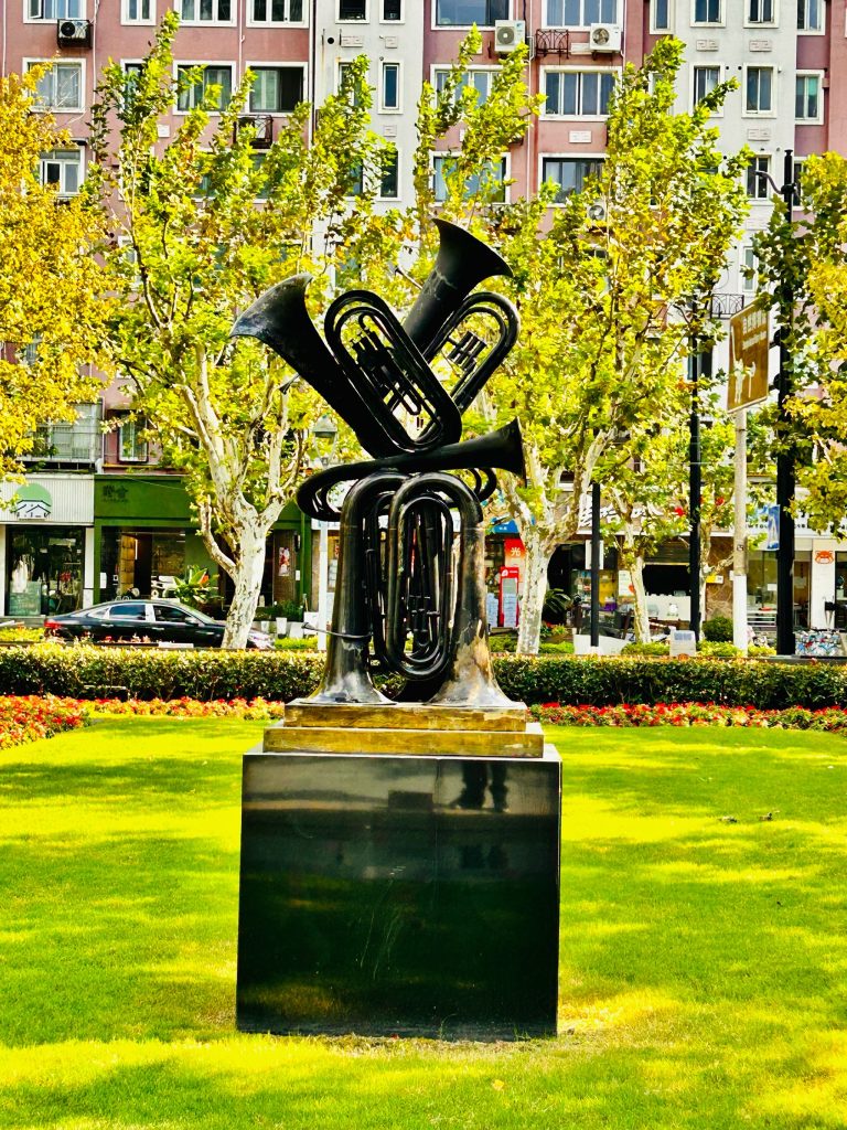 这个雕塑是法国艺术家阿曼（Arman）的作品，名为《交响》（也被称为《管乐交响曲》或《欢乐颂》），属于他标志性的 “堆积艺术” 系列。
这件作品以多件铜管乐器（大号、圆号等）切割堆叠而成，用金属材质凝固住音乐的动感与张力，是上海静安雕塑公园内颇具代表性的音乐主题雕塑。